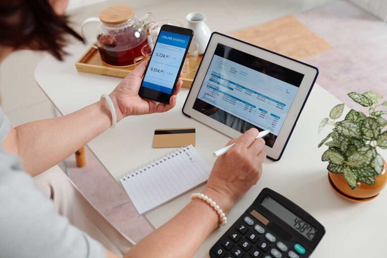 A couple reviews household finances with a calculator and printed bank statements at a kitchen table.